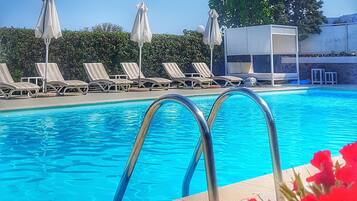 Una piscina con sillas de descanso y sombrillas, rodeada de vegetación.