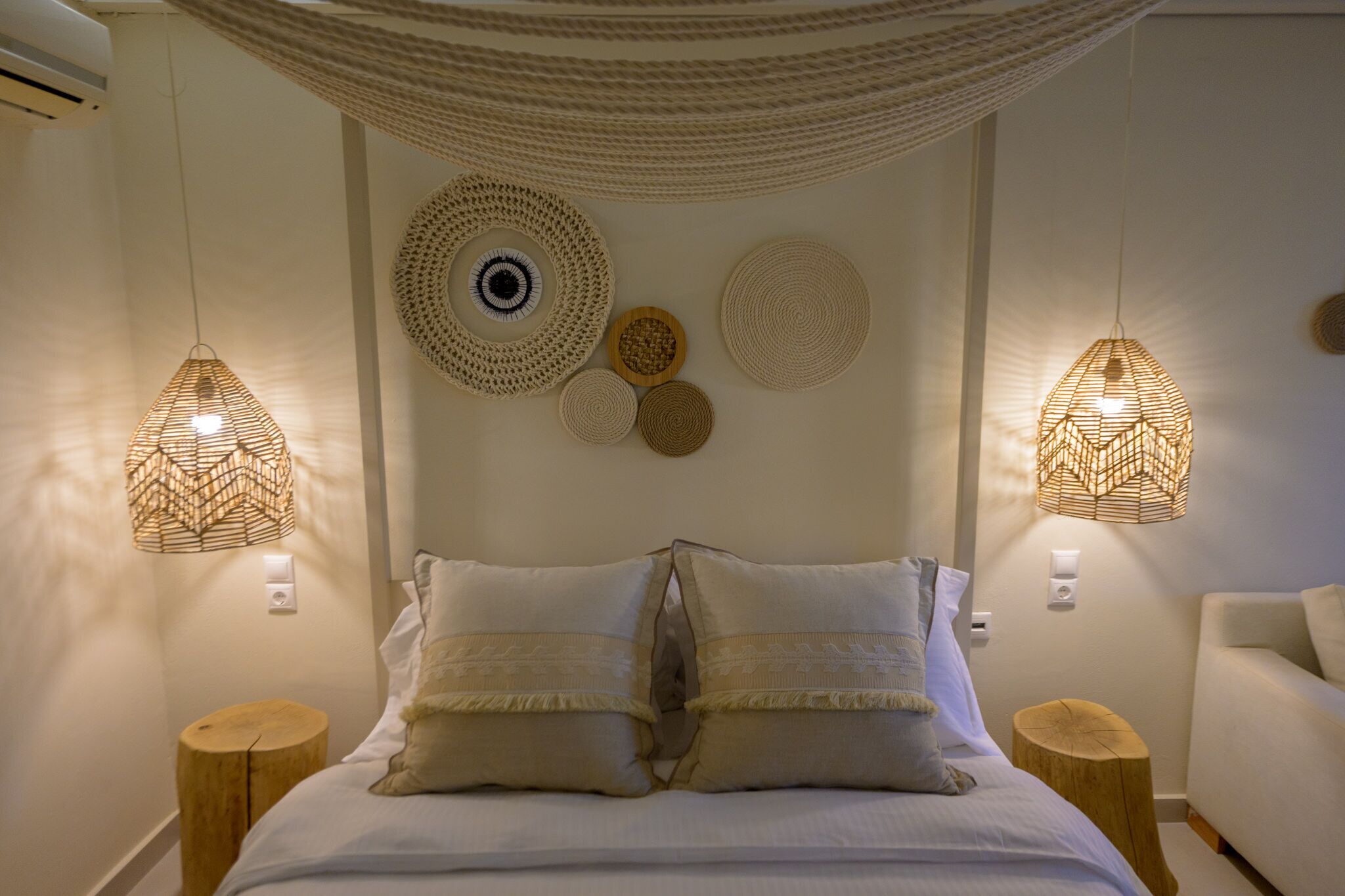 Un dormitorio con cama, dos mesitas de noche, un tapiz de pared tejido y dos lámparas colgantes.