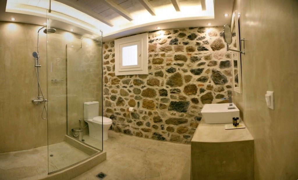 A bathroom with a stone wall, a glass shower enclosure, and a small window.