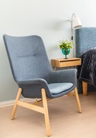 Una habitación moderna con un sillón tapizado gris, una mesita de madera con una planta verde y una lámpara blanca.