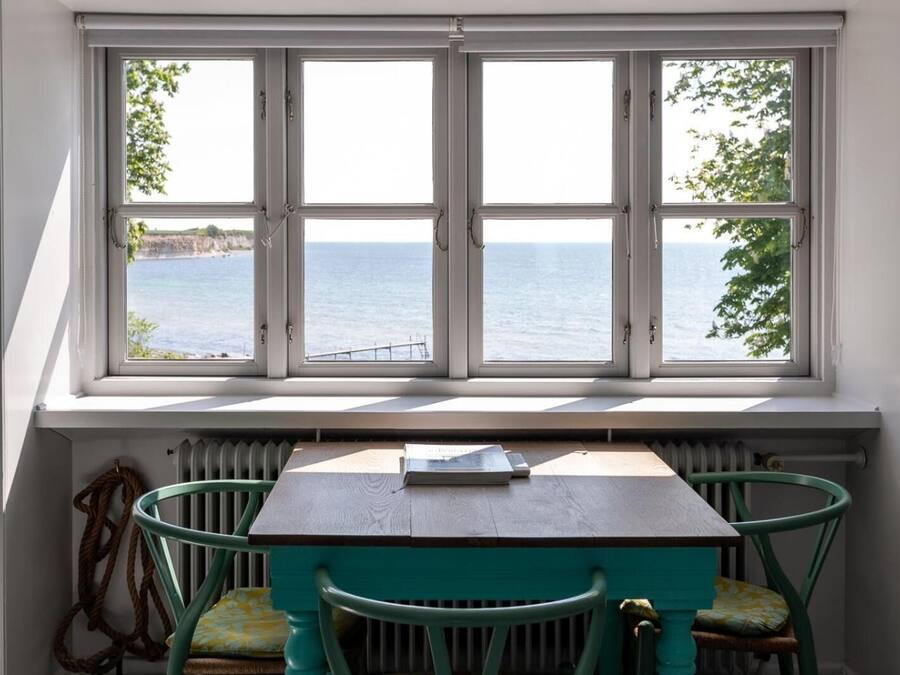 A room with a table and chairs, a view of the sea through a large window, and a radiator below the window.