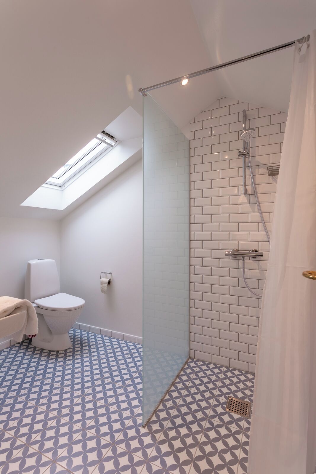 A modern bathroom with a skylight, a shower with a glass door, and patterned floor tiles.