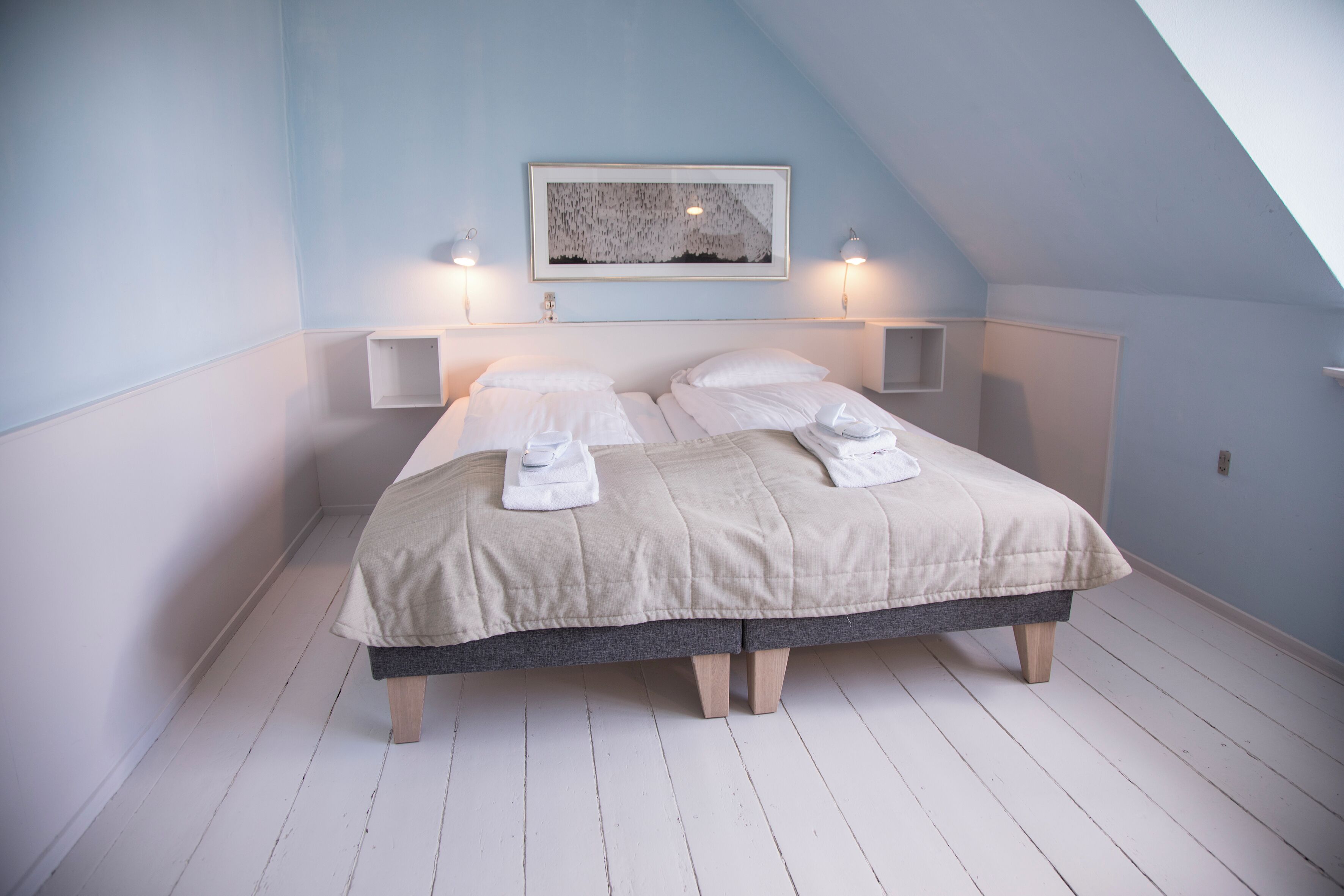 Un dormitorio con una cama, dos mesitas de noche, un estante en la pared y un cuadro enmarcado.