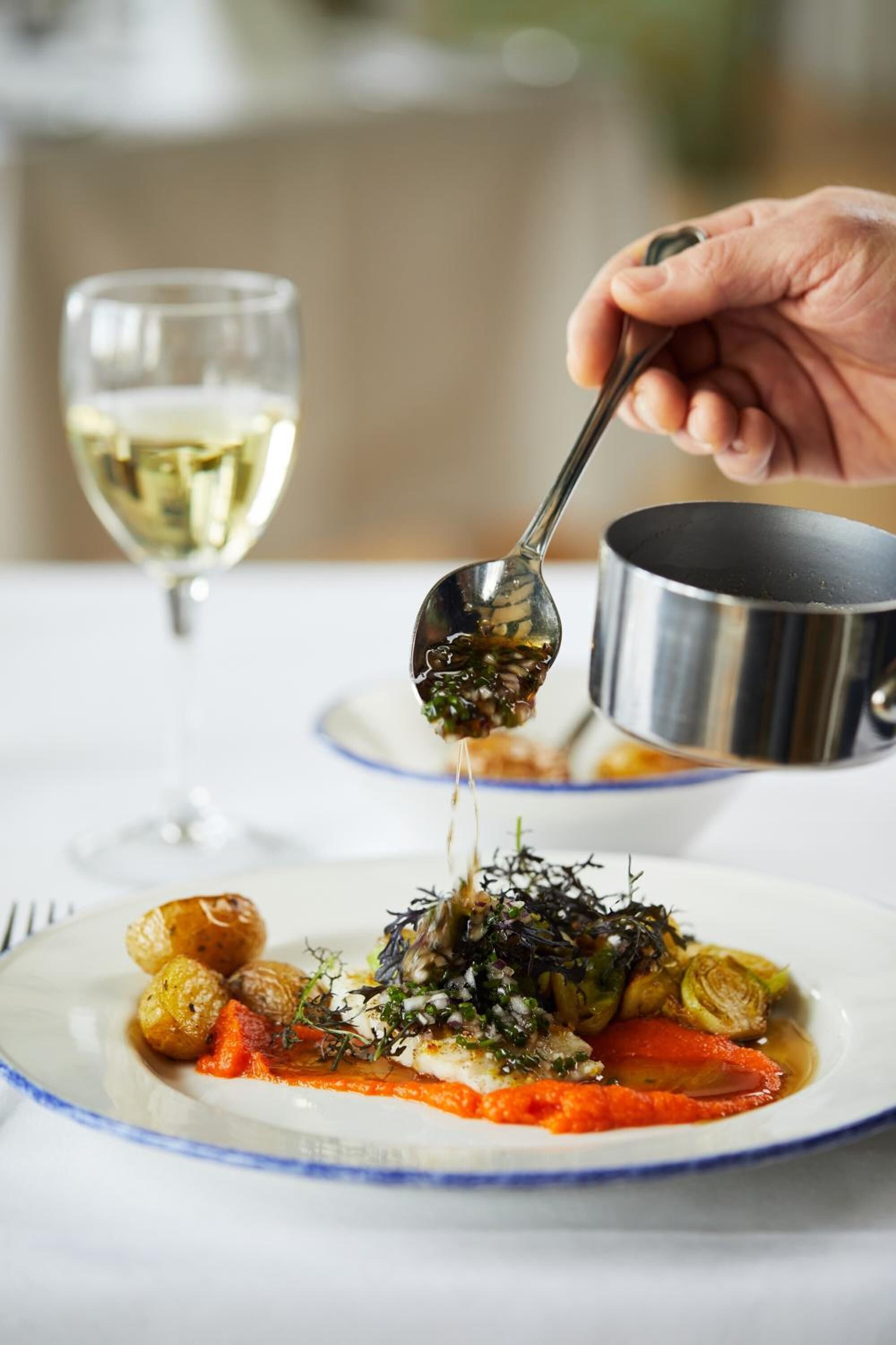 A plate of food with a spoon pouring sauce over it.