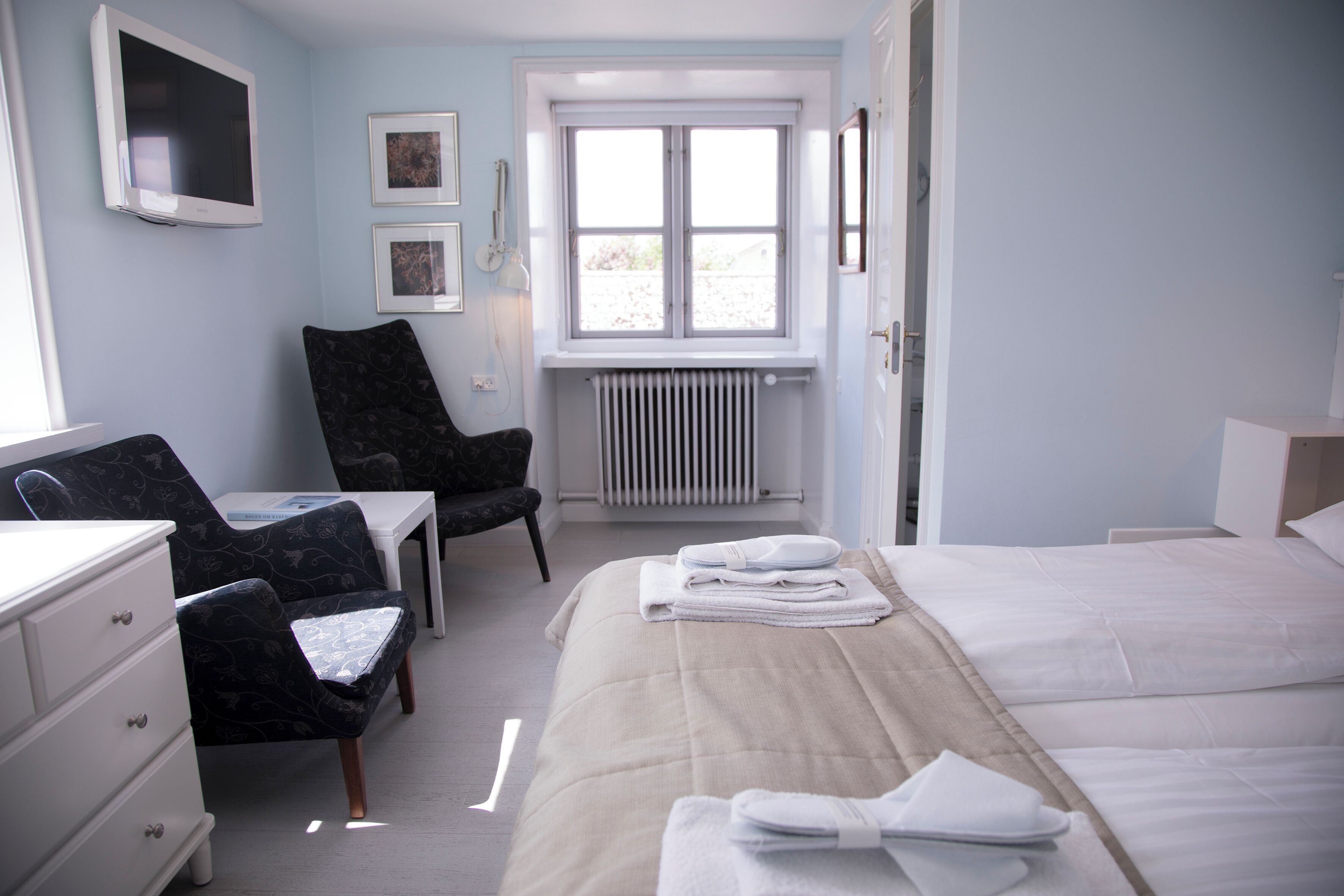 A hotel room with a bed, a desk, a chair, and a radiator.