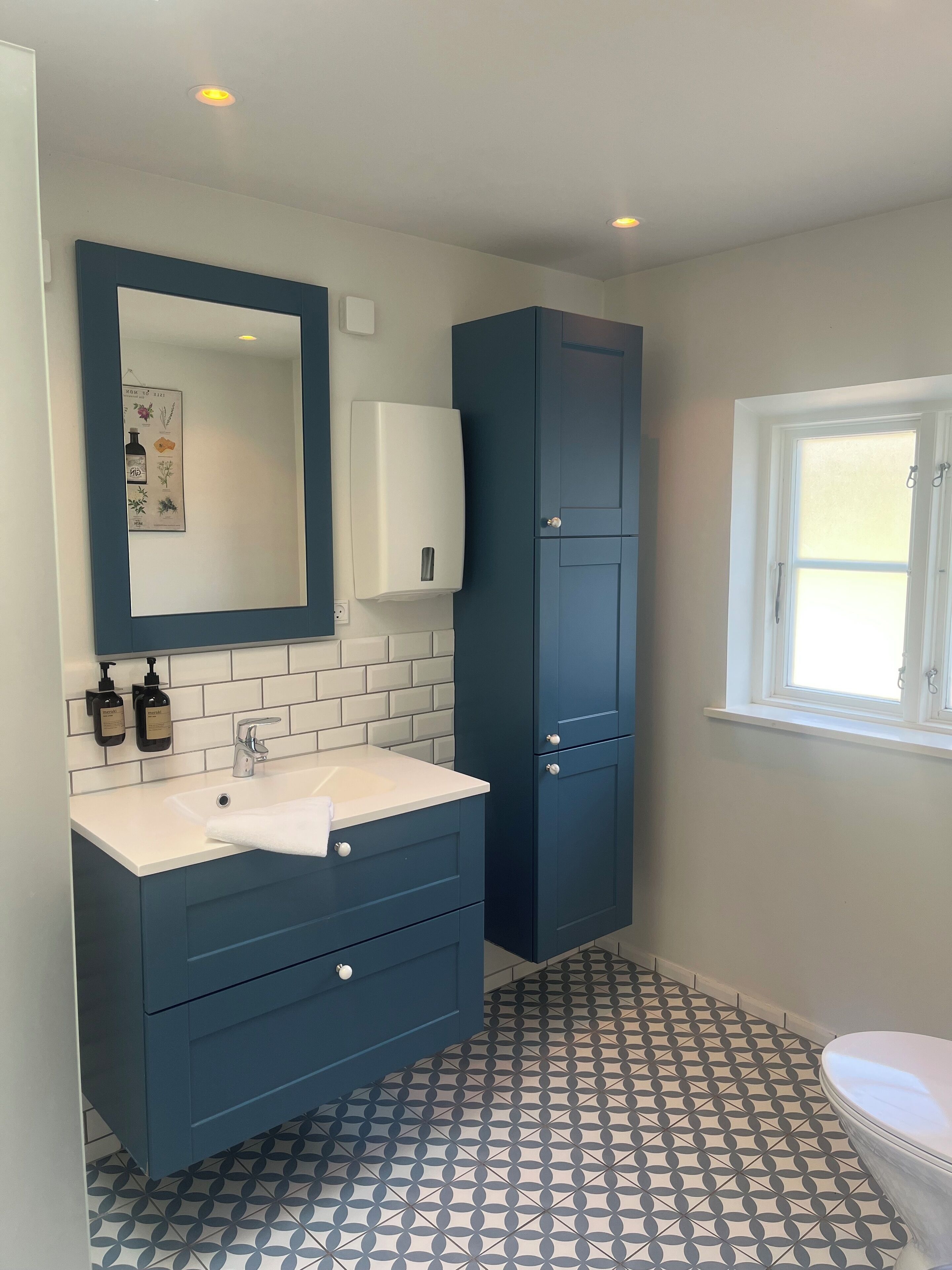 Un baño con lavamanos blanco, armarios azul oscuro, inodoro blanco y baldosas de suelo con diseño.