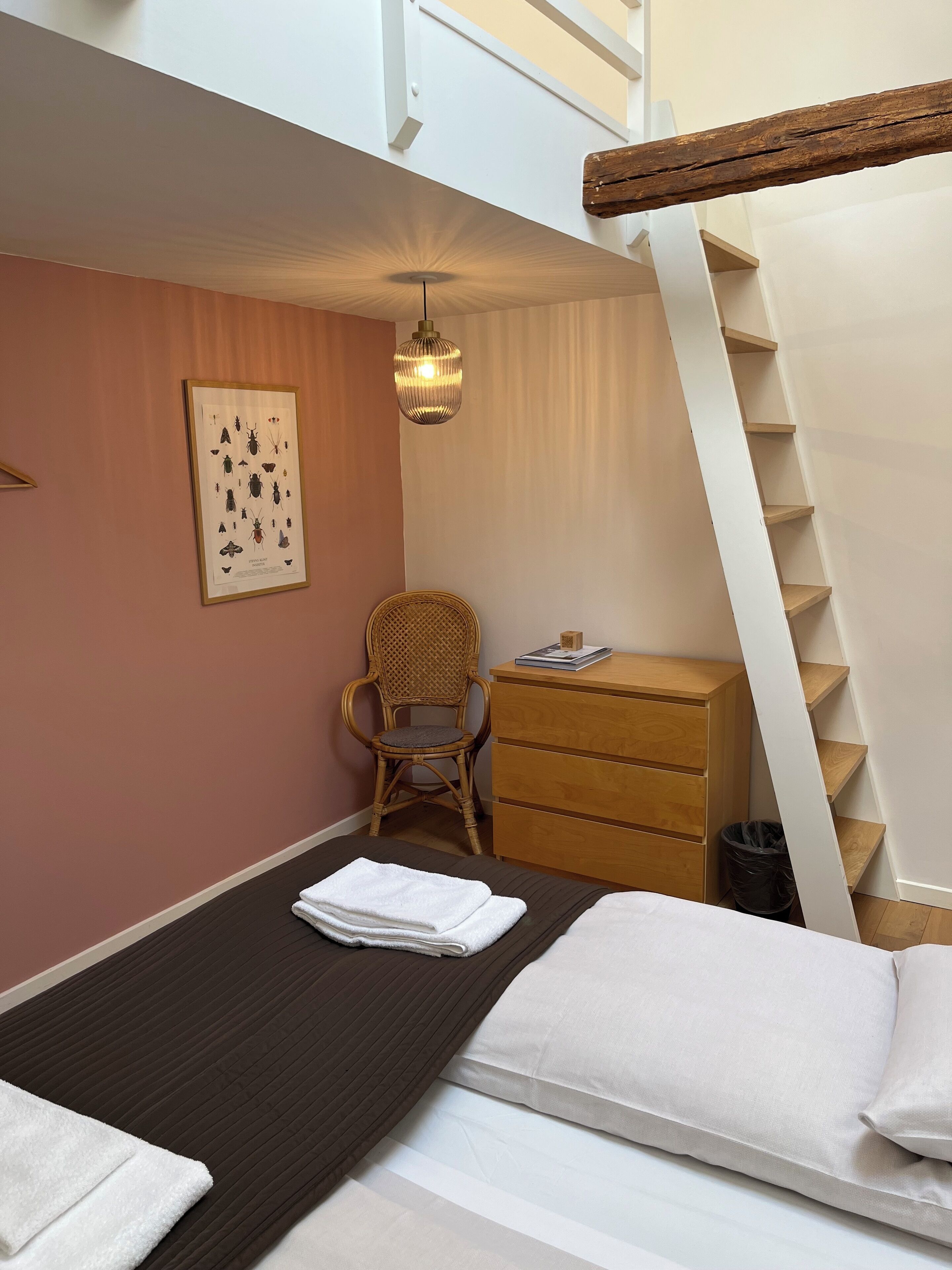 A bedroom with a bed, a chair, a dresser, and a framed insect chart on the wall.