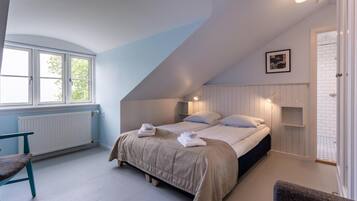A bedroom with a sloped ceiling, a bed with two pillows, a bench, and a radiator.