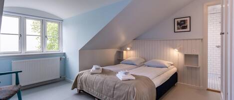 A bedroom with a sloped ceiling, a bed with two pillows, a bench, and a radiator.