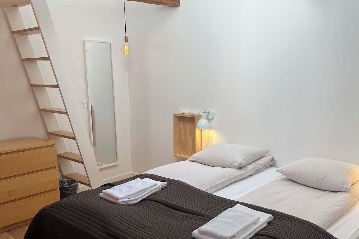 A bedroom with a loft-style ceiling, a bed with white linens, a wooden dresser, and a bedside lamp.
