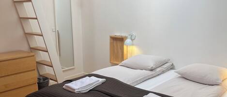 Ein Schlafzimmer mit Schlafgalerie, einem Bett mit weißen Leinen, einer hölzernen Kommode und einer Nachttischlampe.