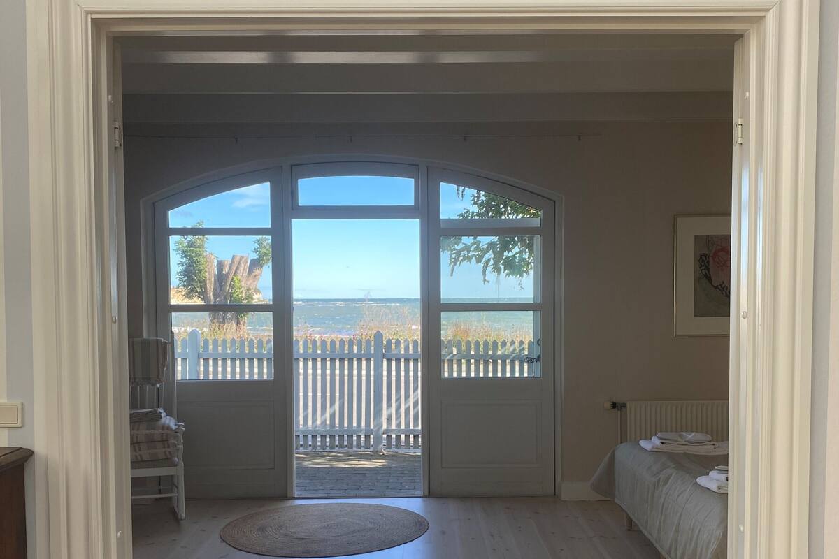 A room with a large arched window, a bed, a radiator, and a framed picture on the wall.