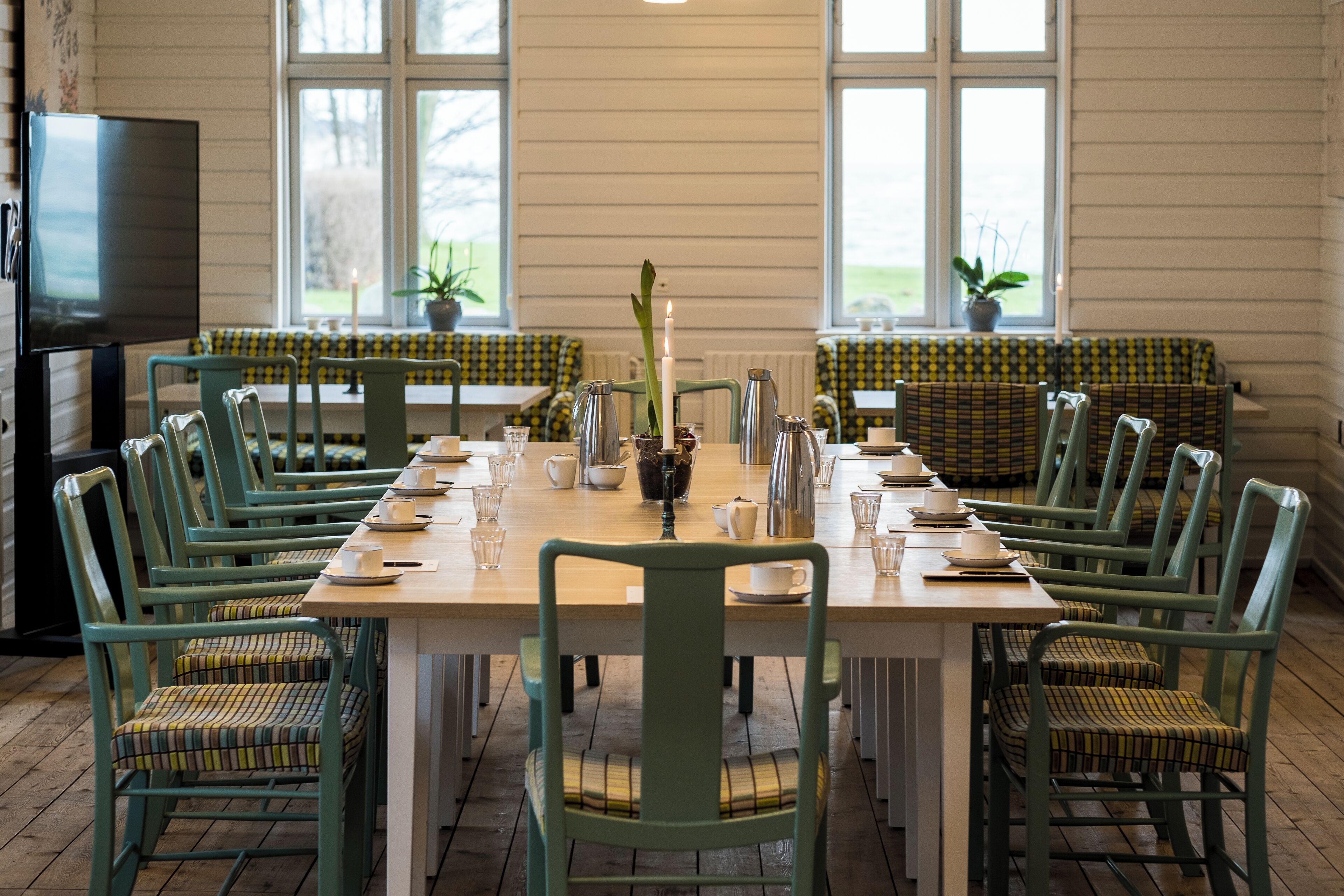 A dining area with a long table set for six, surrounded by green chairs with patterned cushions.