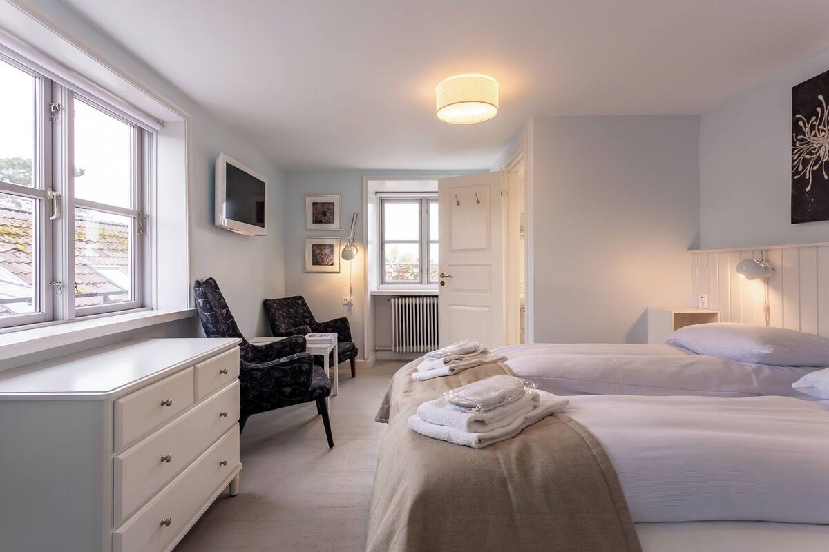 A bedroom with two beds, a desk, chairs, and a radiator.