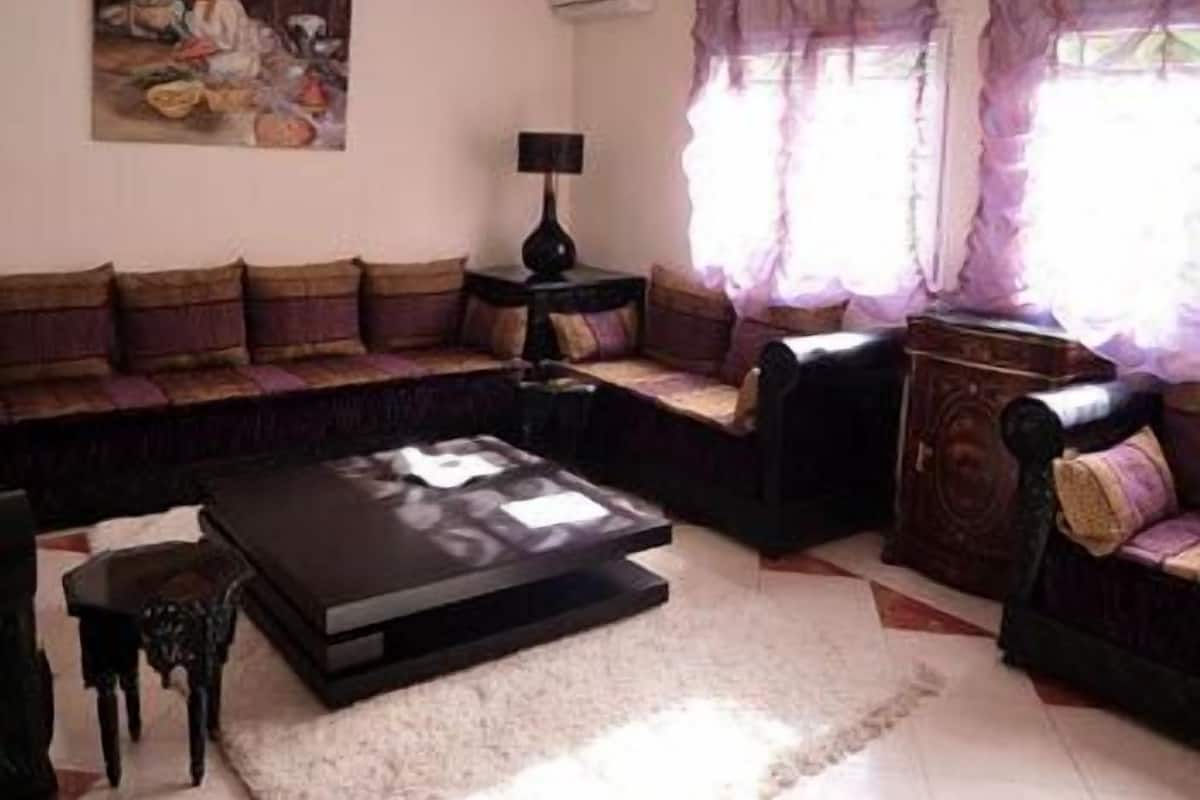 A living room with a sectional sofa, a coffee table, a small table with a lamp, and a painting on the wall.