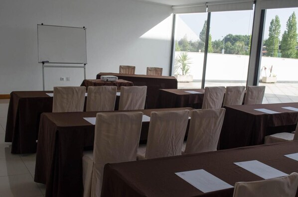 Un salón de conferencias con mesas y sillas, una pizarra y ventanas amplias con vistas a árboles y edificios.