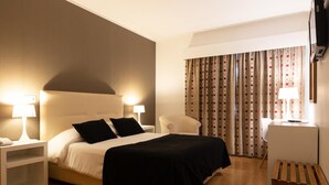 Una habitación de hotel con una cama, dos lámparas de noche, una silla, un escritorio y un televisor.