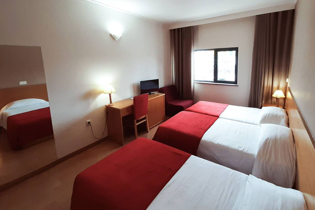 A hotel room with two single beds, a desk with a chair, a television, and a window with curtains.