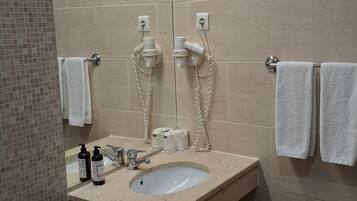 Une salle de bain équipée d’un lavabo, de deux sèche-cheveux et de deux serviettes suspendues à des crochets.