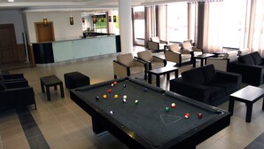 Una mesa de billar con bolas, una recepción y una zona de estar con sillas y mesas.