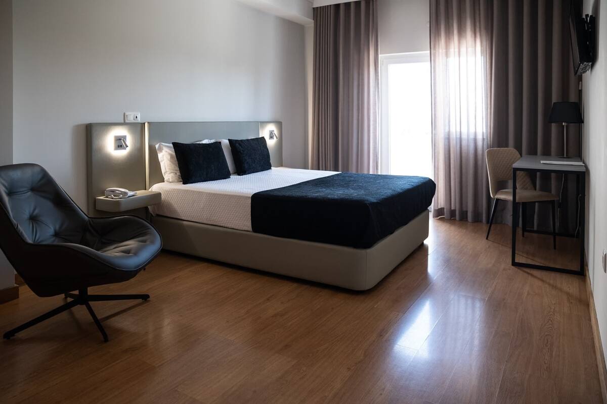 A modern hotel room with a large bed, a desk, a chair, and a lamp.