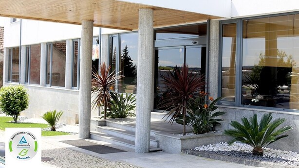 Una entrada de hotel moderna con vestíbulo cubierto, ventanas amplias y plantas de exterior.