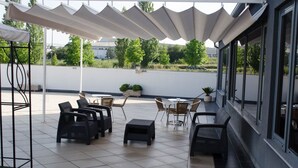 Un espacio al aire libre cubierto con mesas y sillas, una pérgola blanca y vistas al entorno verde.