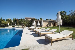 A poolside area with lounge chairs and umbrellas, a clear sky, and a building in the background.