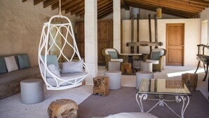 A rustic interior with a hanging chair, a glass-top table, and a wooden bench.