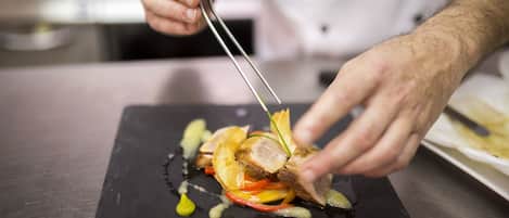 A chef using tongs to plate a dish on a black slate.