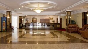 A spacious lobby with a polished marble floor, a grand chandelier, and leather seating.