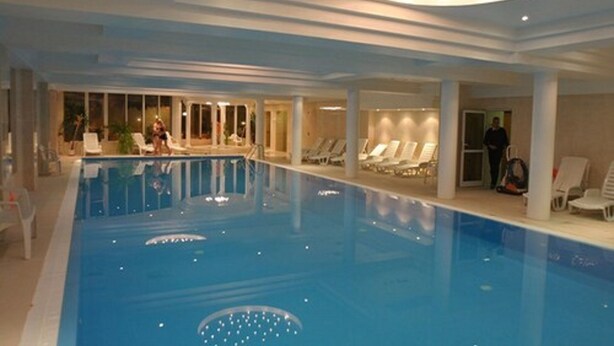 An indoor swimming pool with clear water, surrounded by lounge chairs and a ceiling with recessed lighting.