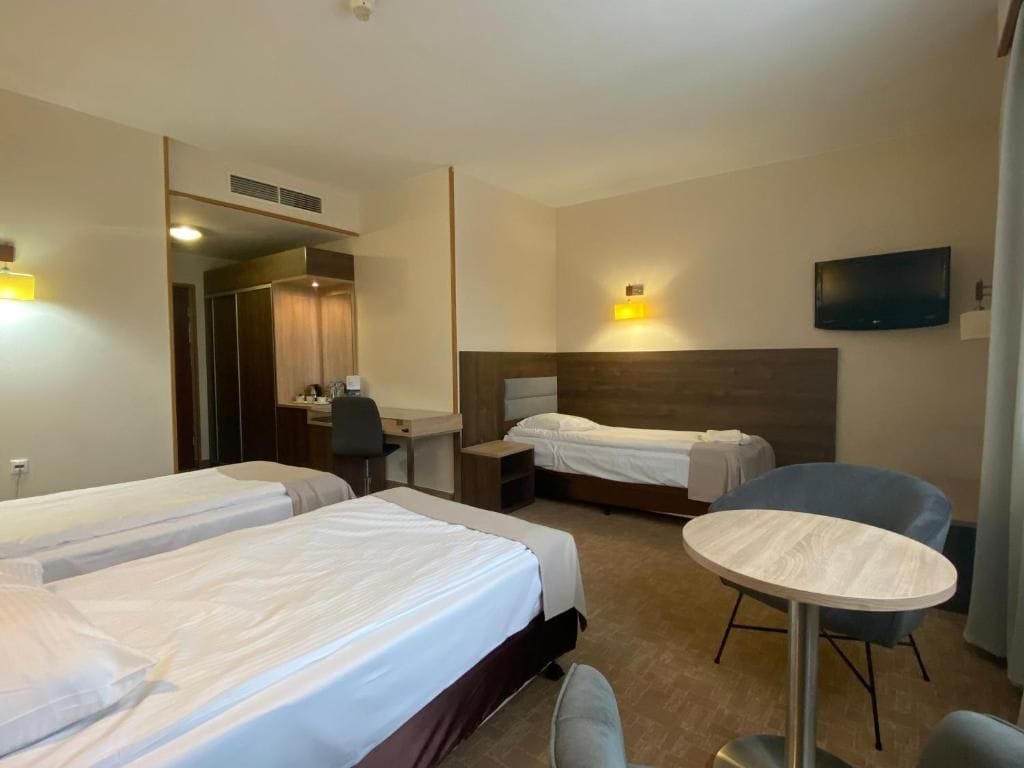 Habitación de hotel con dos camas, un escritorio, una silla, una mesa redonda y un televisor.
