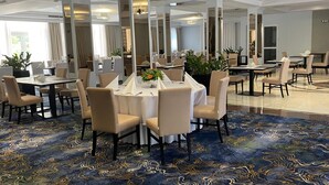 A hotel dining area with round tables, beige chairs, and a blue patterned carpet.
