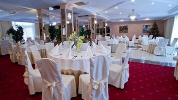 A banquet hall with round tables, white chairs, and a red carpet.
