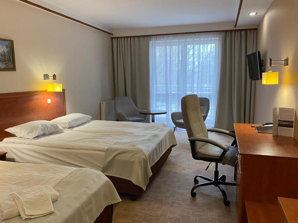 A hotel room with two beds, a desk, a chair, and a television.