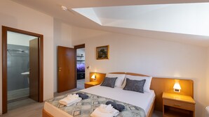 Habitación de hotel con cama, dos mesitas de noche con lámparas, cabecero de madera, un cuadro en la pared y baño a la vista a través de una puerta abierta.