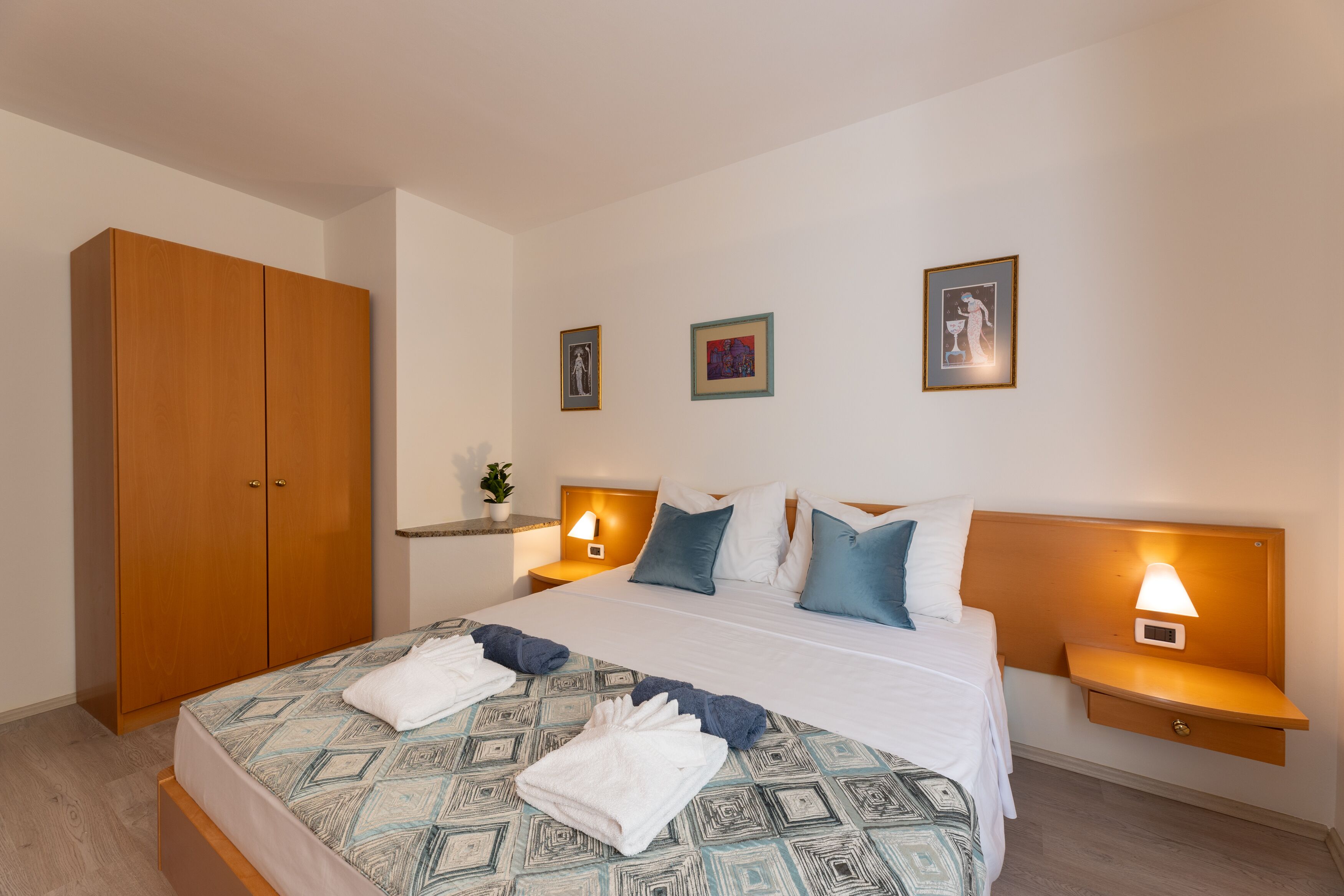 A hotel room with a bed, nightstands, a wardrobe, and wall art.
