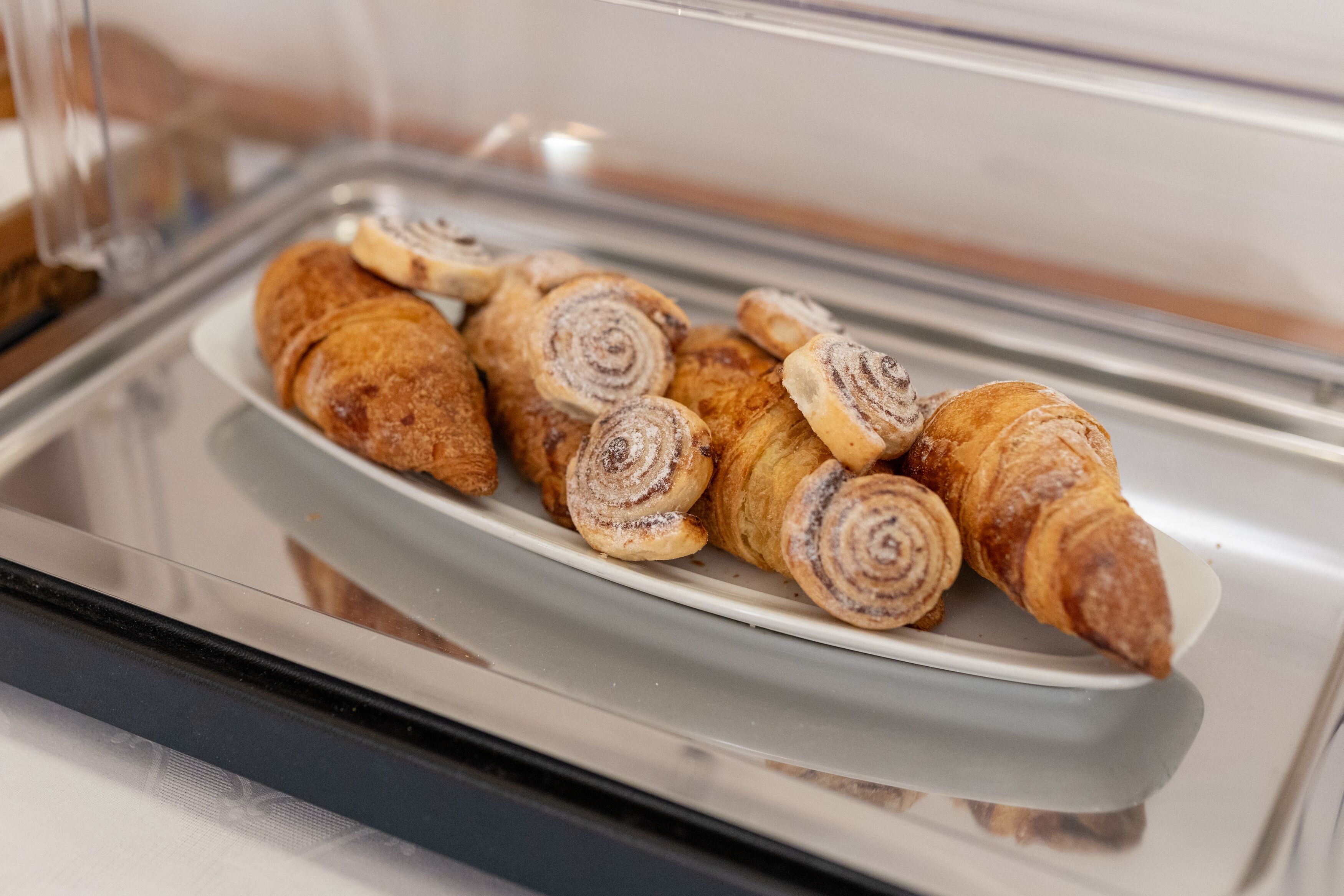 A display case containing various pastries, including croissants and cinnamon rolls.