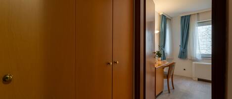 A room with a wooden wardrobe, a dining table with chairs, a potted plant, and a window with curtains.