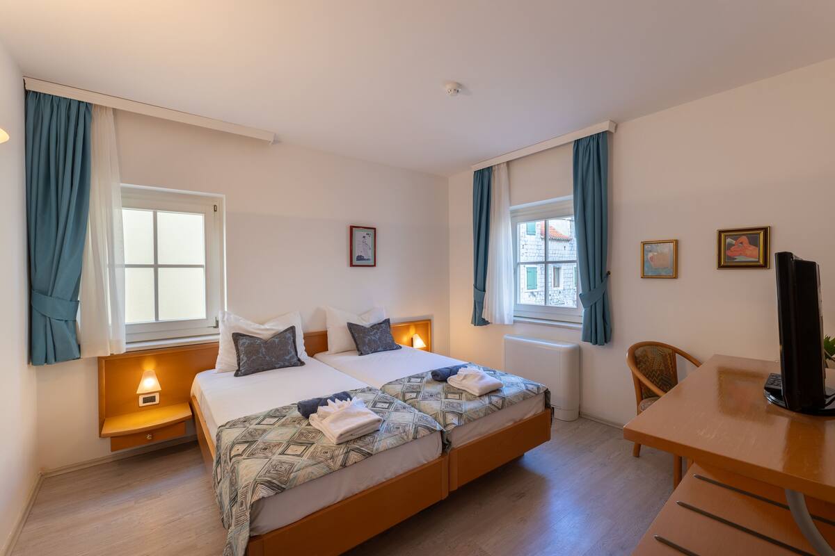 A double bed with a patterned duvet, bedside lamps, a desk with a computer, and a chair.