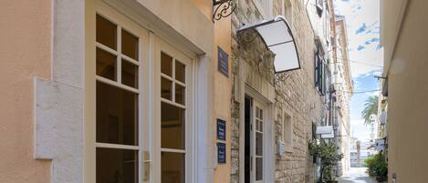 A narrow alleyway with a building featuring a large white door and a small window.