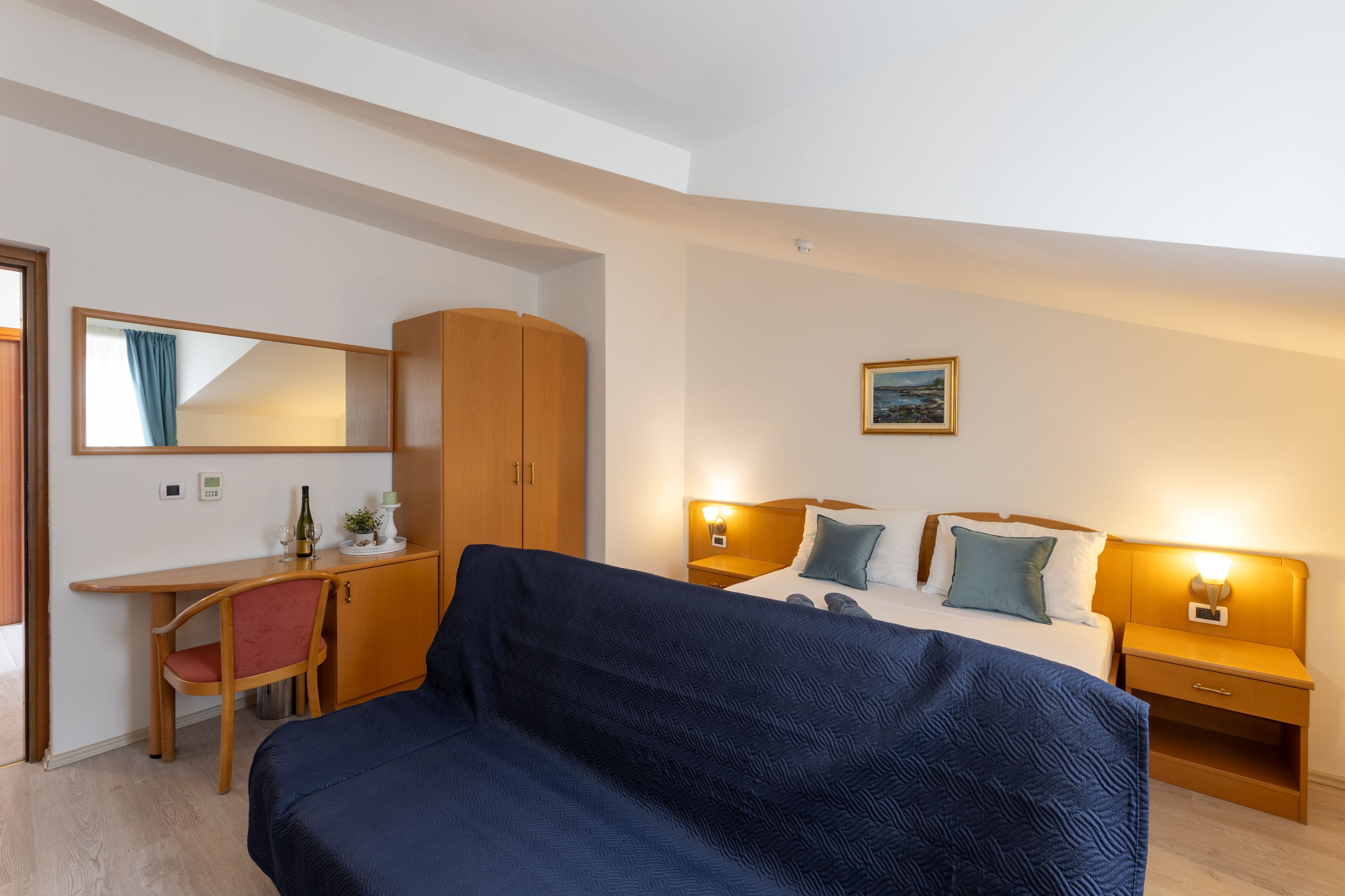 Een hotelkamer met een bed, een bureau, een stoel, een kledingkast en een nachtkastje met een lamp.