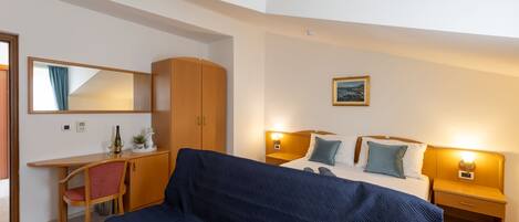 A hotel room with a bed, a desk, a chair, a wardrobe, and a nightstand with a lamp.