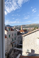 A stone building with a red-tiled roof, a staircase, and a view of a town with mountains in the background.