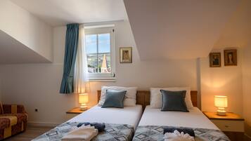 A hotel room with two beds, a window with curtains, a nightstand with a lamp, and a painting on the wall.