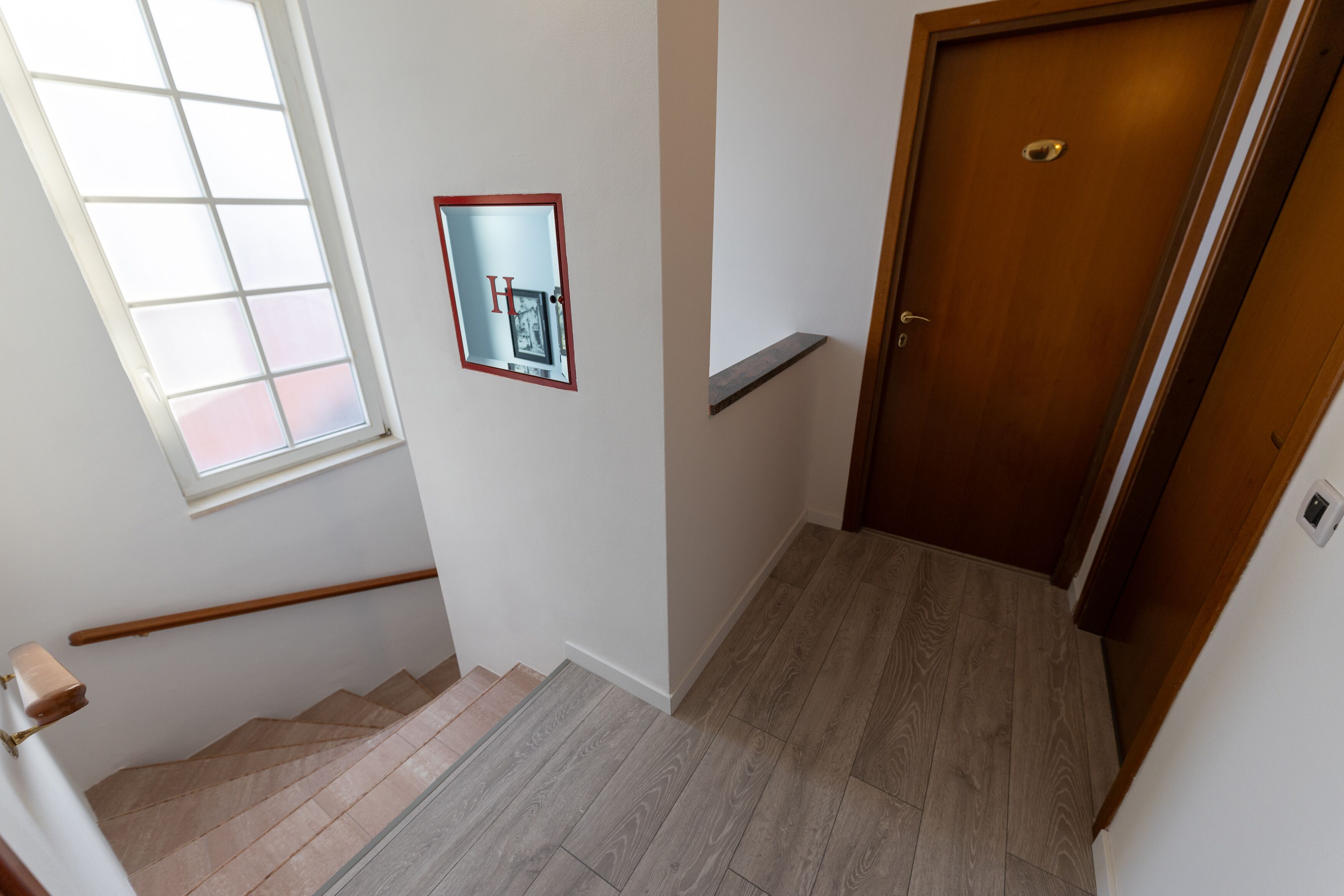 A staircase with a wooden handrail, a wooden door, and a small window with a picture frame.