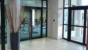 Eine geräumige Lobby mit einer großen Säule, einer Glastür zum Fitnessbereich und einem gefliesten Boden.