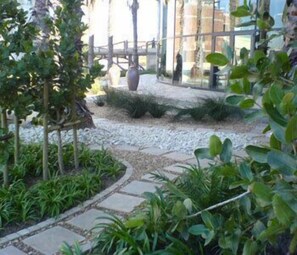 A garden pathway with stone tiles, surrounded by various plants and a large vase.