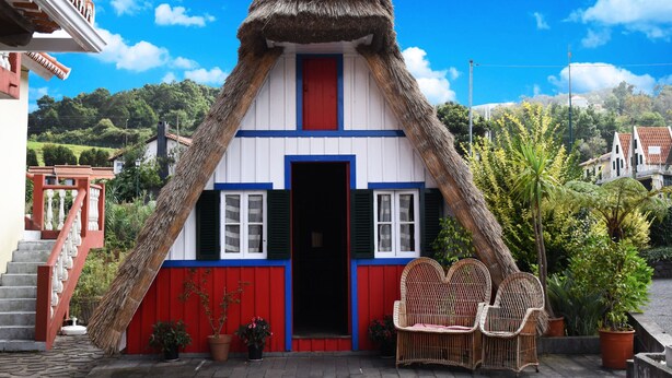 Una casa tradicional con techo de paja, puerta roja y fachada blanca y azul.